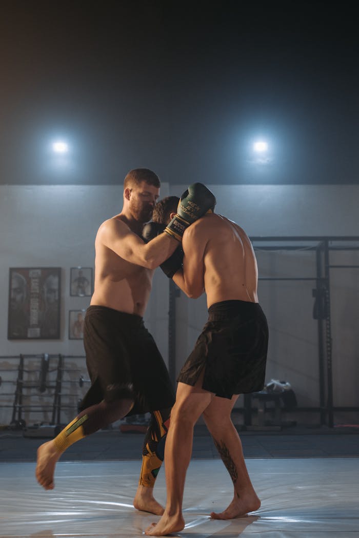Services Two shirtless male fighters practicing martial arts in a dimly lit gym.