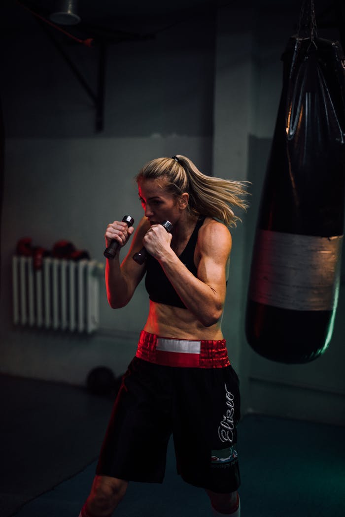 Strong female boxer training indoors with a punching bag, showcasing power and focus.